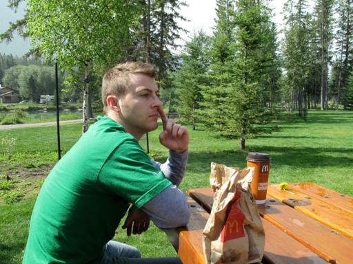 man wearing green shirt, sitting in the park with foods from McDonalds on the table