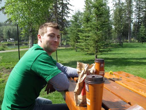 man wearing green shirt, sitting in the park smiling at the camera