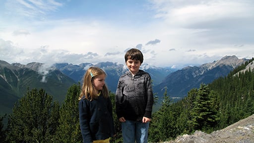 two little kids standing with the mountain and green trees background