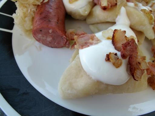 white plate with perogies, fried bacon and onions, with kolbasa and sauerkraut