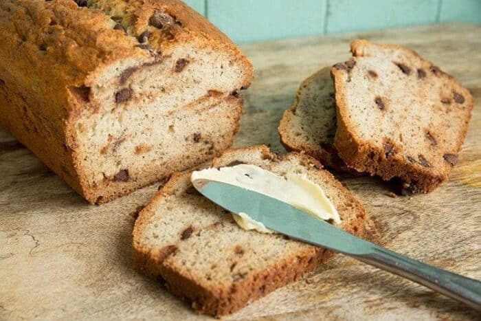 a slice of Banana bread slathered with butter on top using a spread knife