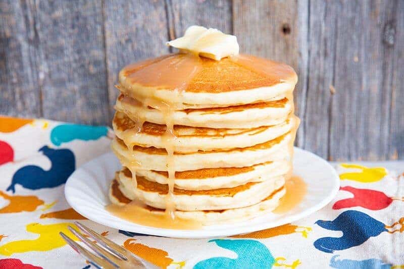 stack of pancakes in a white plate with butter and syrup