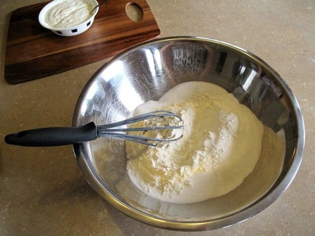 a whisk on dry mixture for scones in a large stainless bowl