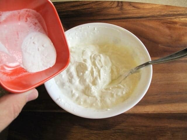 adding the baking soda to a bowl of sour cream in a white bowl