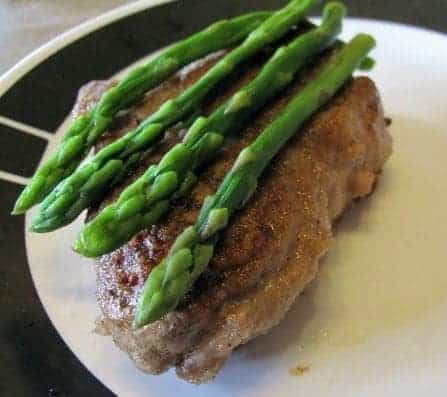 4 spears of asparagus across the steak in a white plate