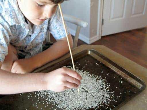a kid doing an art with the sesame seeds in the tray