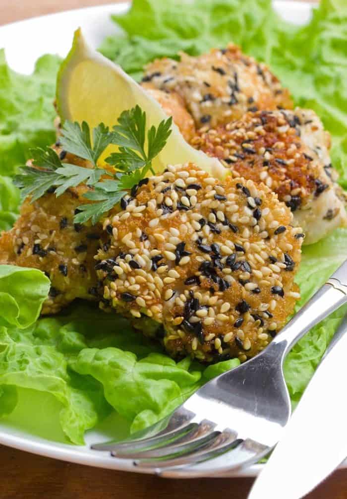 Baked Sesame Chicken Strips on a plate lined with lettuce leaves, garnish with parsley and lemon slice