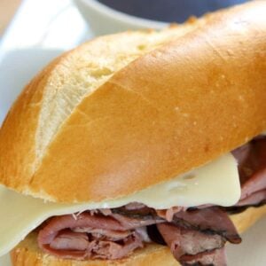 crock pot beef dips sandwich with melty slice of Swiss Cheese and a cup of Au Jus on side