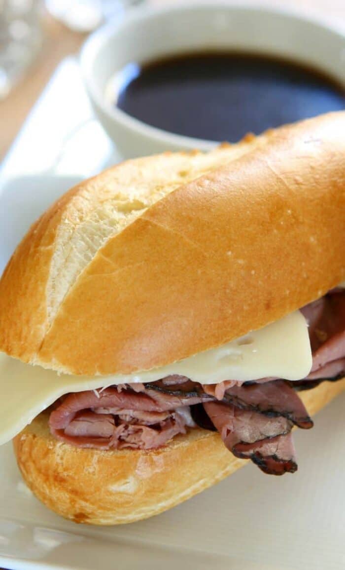 crock pot beef dips sandwich with melty slice of Swiss Cheese and a cup of Au Jus on side