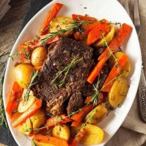 large white oval plate with Pot Roast in the center surrounded by different vegetables