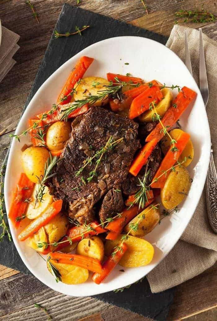 large white oval plate with Pot Roast in the center surrounded by different vegetables