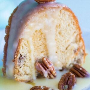 white dessert plate with a slice of Pecan Butter Rum Cake topped with icing and some pecans