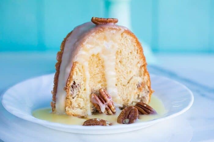 white dessert plate with a slice of Pecan Butter Rum Cake topped with icing and some pecans