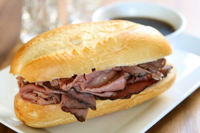 crock pot beef dips sandwich in a white rectangular plate with a cup of Au Jus