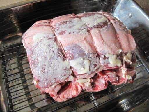 prime rib roast covered with butter in a wire rack with a deep pan to catch the drippings