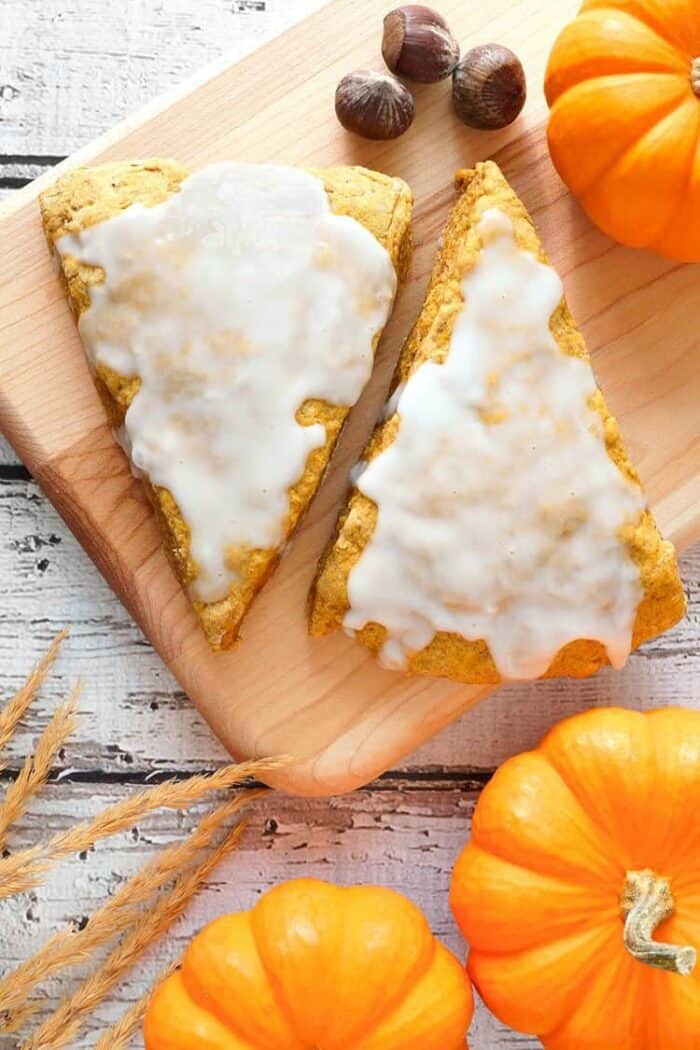 glazed slices of Pumpkin Scones on wood board, pumpkins and nutmegs beside it