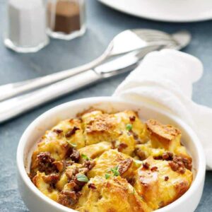 Sausage Breakfast Bake Casserole in a small white round baking dish. Fork, bread knife, salt and pepper shakers on background