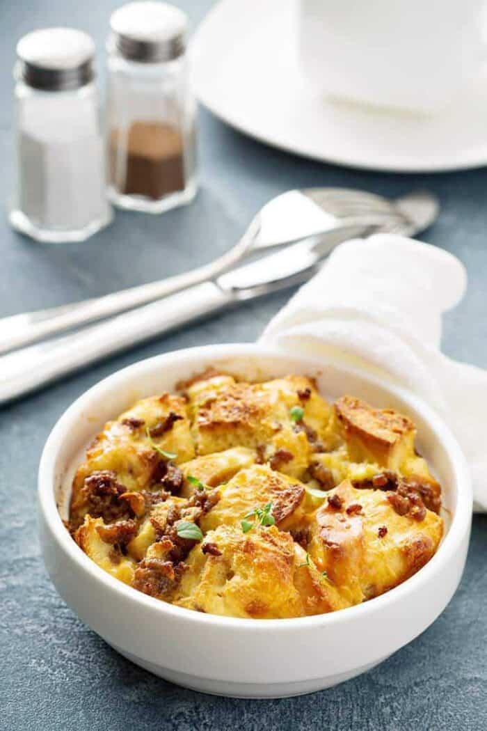 Sausage Breakfast Bake Casserole in a small white round baking dish. Fork, bread knife, salt and pepper shakers on background