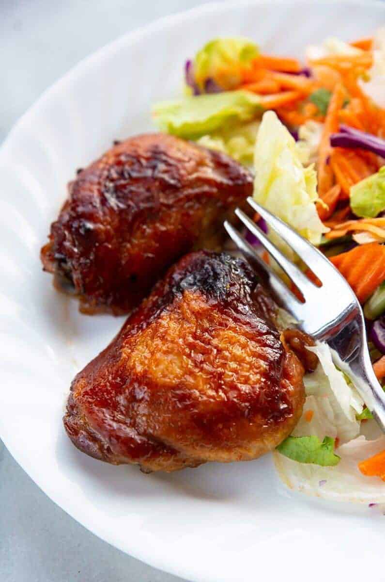close up baked Teriyaki Chicken on a white plate with a fork and some vegetables
