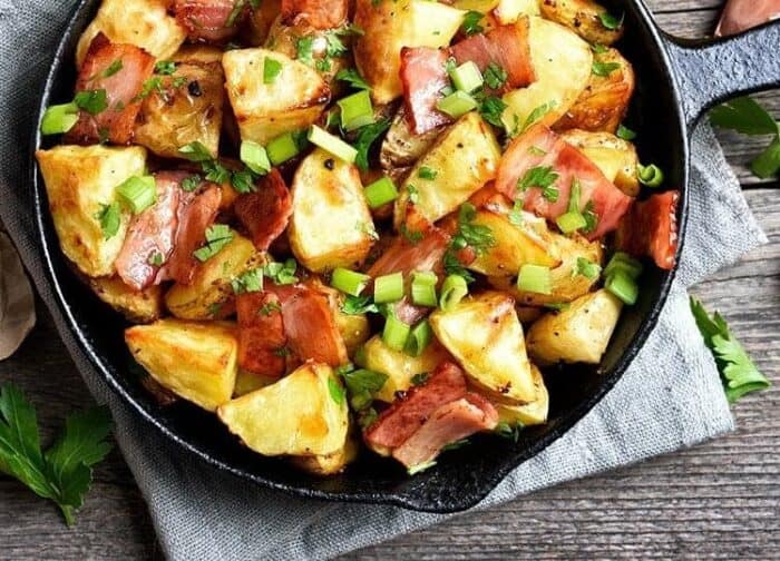 delicious skillet fried potatoes with bacon and green onions garnished with parsley placed on a light blue cloth on top of the table