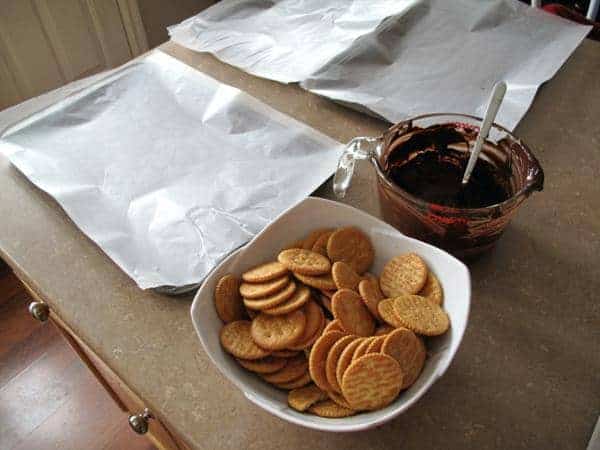 2 baking sheets with parchment paper, melted chocolate chips in Pyrex glass and a bowl of Ritz crackers