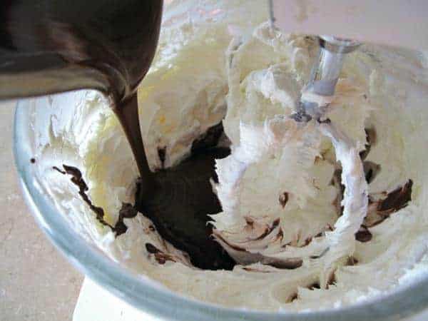 Pouring the melted chocolate into the cream cheese mixture in the bowl,