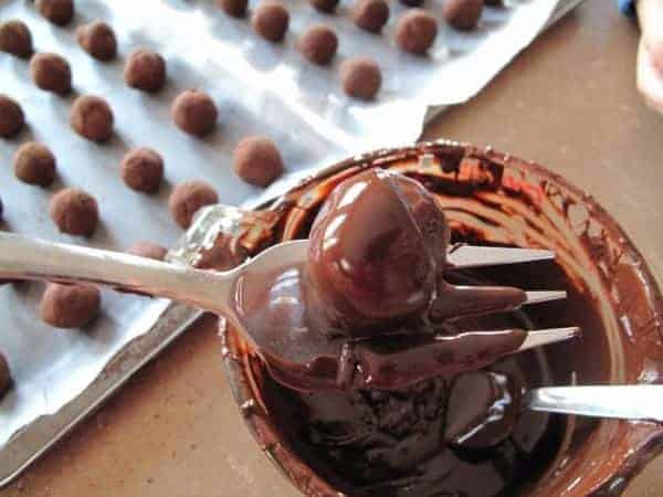dipping each ball of chocolate truffles into the melted chocolate using a fork