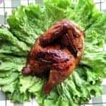 close up Honeyed Cornish Game Hens in a green checkered plate garnish with some lettuce leaves
