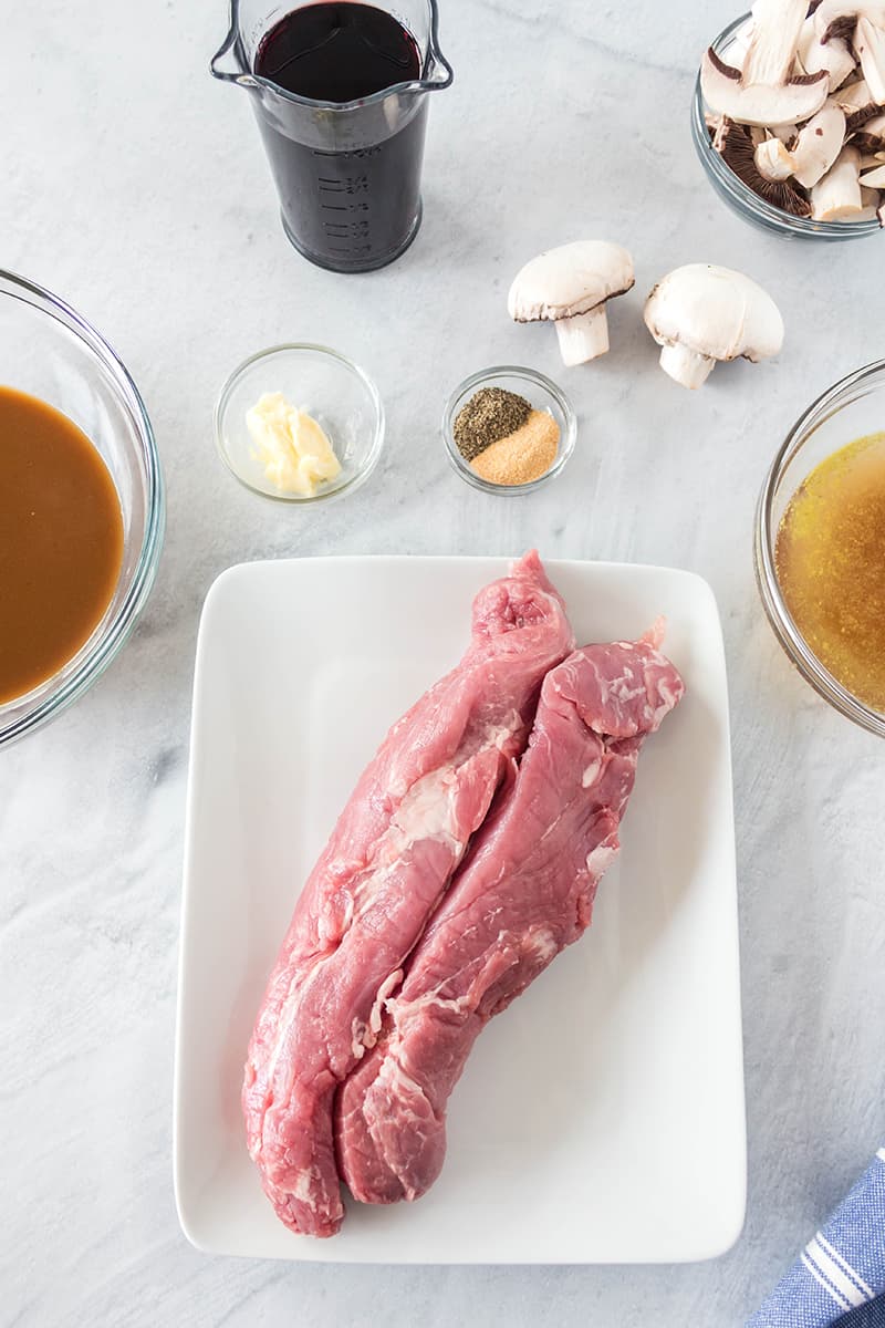 raw pork tenderloing, mushrooms, gravy, red wine, beef broth, butter, salt and pepper on a white marble board