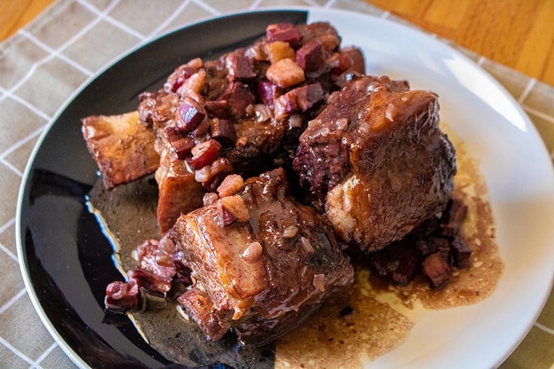 4 pieces of Braised Beef Short Ribs in a black and white serving plate