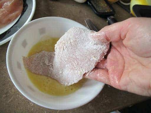 dipping the chicken with flour into beaten egg on white bowl