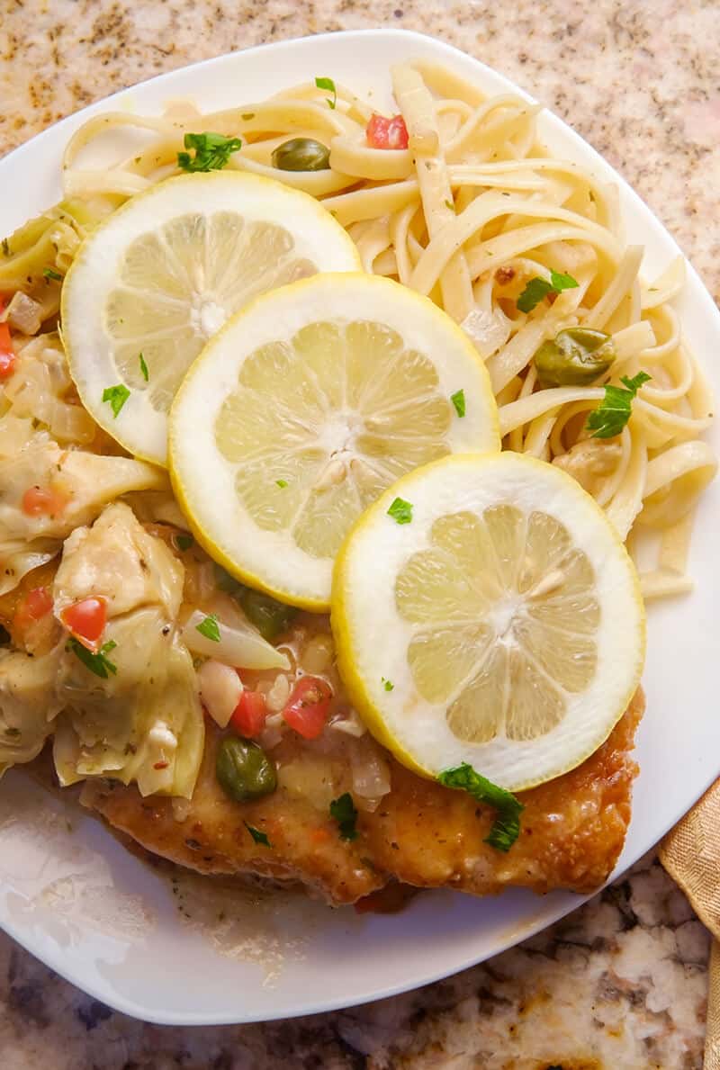 top down shot of Chicken Francaise served over pasta, topped with lemon and parsley