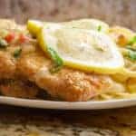 Chicken Francaise over pasta topped with slices of lemon and fresh parsley