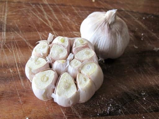 2 garlic heads in wood board, one garlic head with exposed cloves