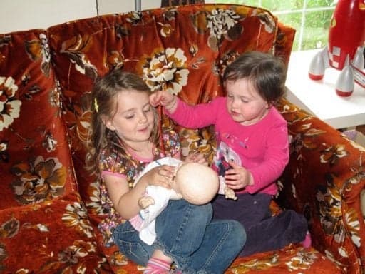 two little kids playing the baby doll in the couch