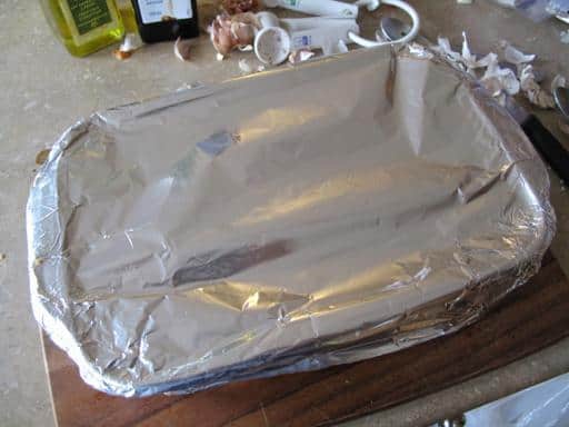 garlic heads with olive oil in a baking sheet covered with tinfoil ready for roasting