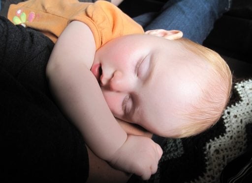 little baby in orange shirt sleeping at the arms of her mother