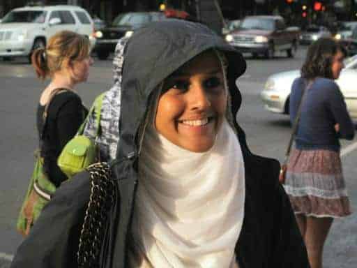 a girl with a smile wearing black jacket with hood and white scarf-type wrap on her neck