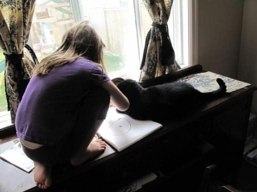little girl doing her drawing with a cat beside her