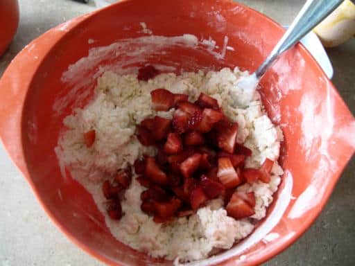 Strawberries added to the combined wet and dry ingredients for Strawberry Yogurt Scones in an orange mixing bowl