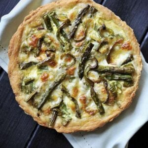 white cloth underneath a whole Swiss Mushroom Asparagus Quiche on a dark wood background