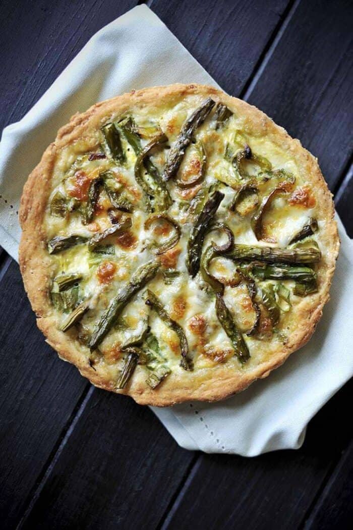 white cloth underneath a whole Swiss Mushroom Asparagus Quiche on a dark wood background