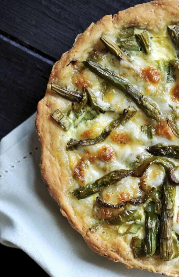 close up Swiss Mushroom Asparagus Quiche with lovely pasta crust on a white cloth and dark wood background