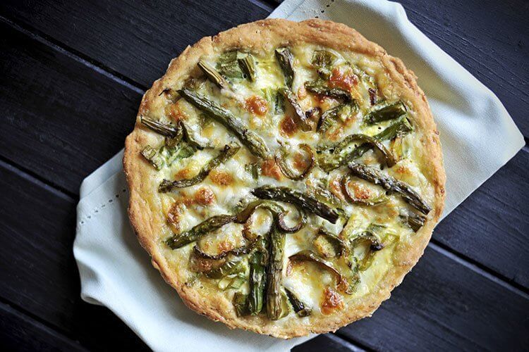 a whole Swiss Mushroom Asparagus Quiche on a white kitchen cloth