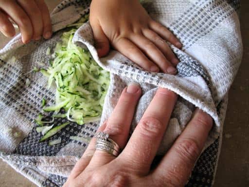 hands of a child and mother on a clean tea towel with shredded zucchini