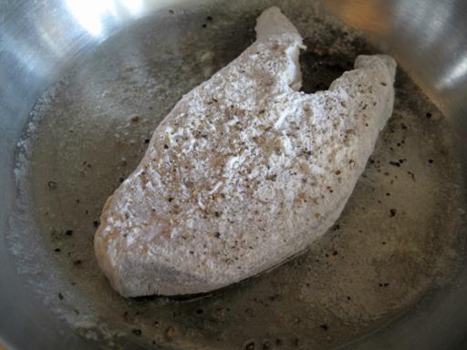 frying a raw halibut steak in a frying pan with melted butter