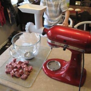 meat grinder attached to the mixer, cube sliced meat and a bowl on the table