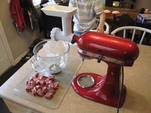 meat grinder attached to the mixer, cube sliced meat and a bowl on the table