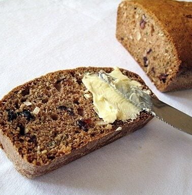 spreading some butter into a slice of Cranberry Coconut Zucchini Loaf using a spread knife