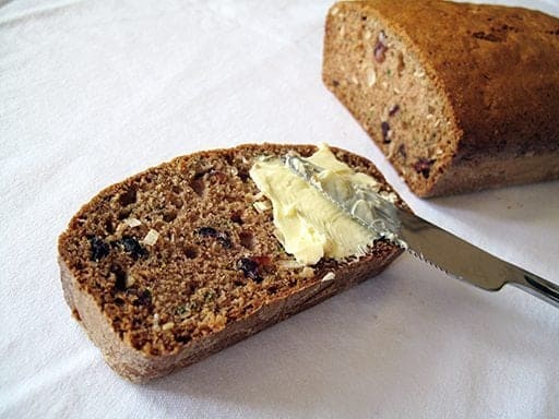spreading some butter into a slice of Cranberry Coconut Zucchini Loaf using a spread knife